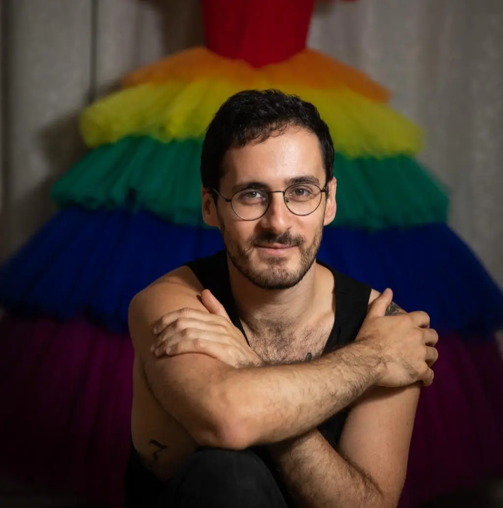 תמונת פורטרט של מתן אנחיסי, מרצה במחלקה לעיצוב אופנה. מתן נראה כאשר מאחוריו שמלה עם חצאית בצבעי הקשת